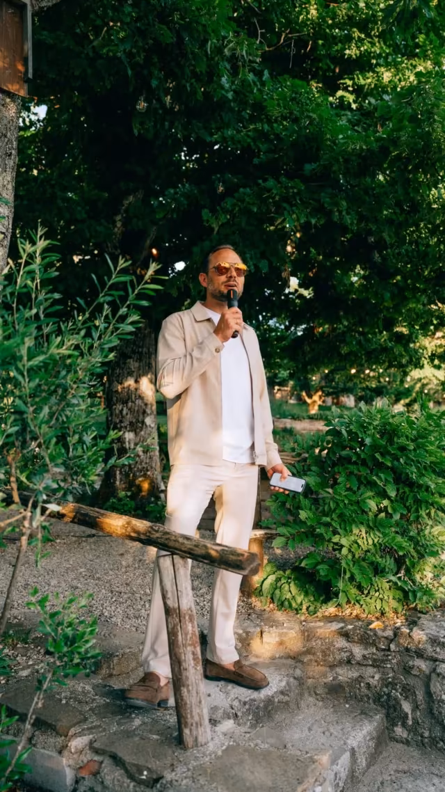 Een presentator met microfoon spreekt de groep toe in een tuin